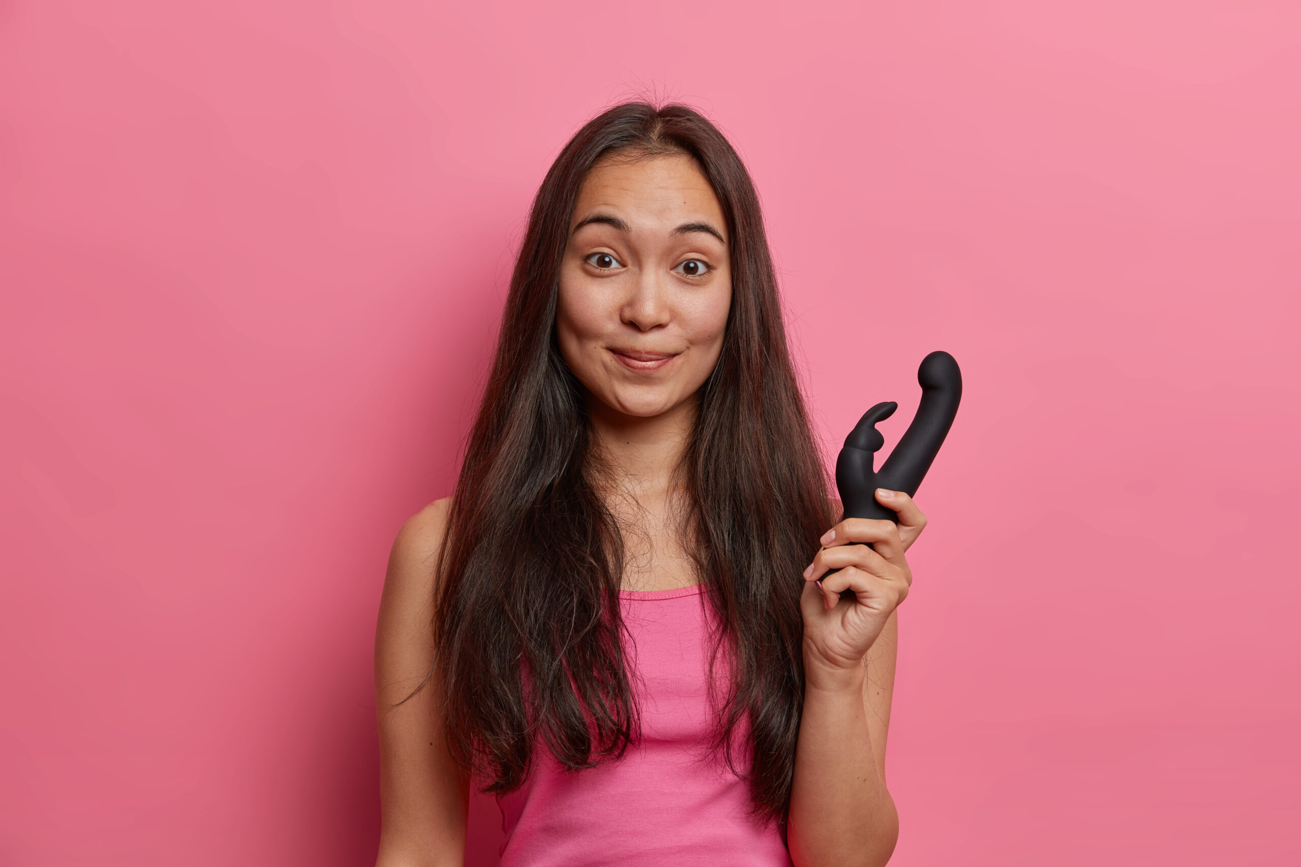 Pleased woman with eastern appearance holds dildo in form of rabbit uses vibrator to massage clitor buys sex toys for pleasuring herself and feeling enjoyment gets orgasm easier replaces partner | pleasurable A woman holding a dildo
