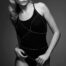 Black-and-white photo of a woman wearing a delicate silver body chain over a black sleeveless bodysuit.