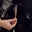 Close-up of a hand pulling a metal zipper on a shiny black jacket, halfway zipped down the front