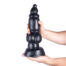 Large black silicone dildo held upright by two hands against a white background.