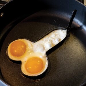Two sunny-side-up eggs cooking in a heart-shaped egg ring on a frying pan.