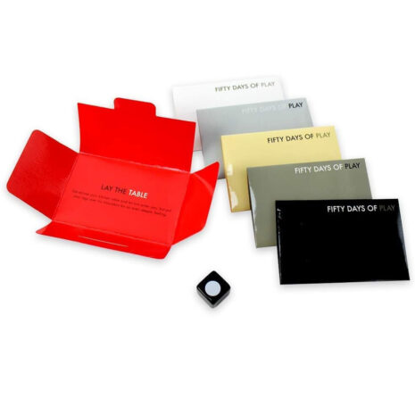 FIFTYDAYx3jpg Red open box with 'LAY THE TABLE' text; beside it six 'FIFTY DAYS OF PLAY' cards in white, cream, gray, yellow, olive, and black, plus a small black die.