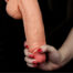 Close-up of a hand gripping a penis against a dark background, showing tight grip and skin textures.